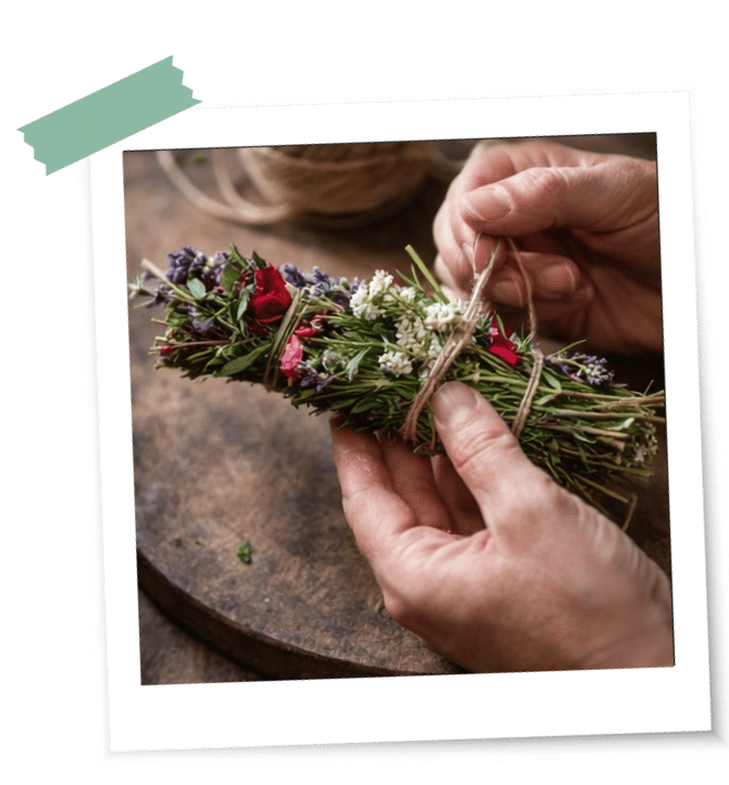 Blumen und Kräuter werden mit einem Faden von einer Hand zu einem Räucherstick gebunden für ein Ritual