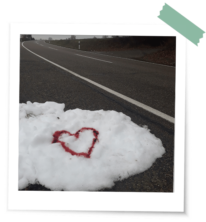 Ein rotes Herz aus Blut im Schnee am Rand einer Straße