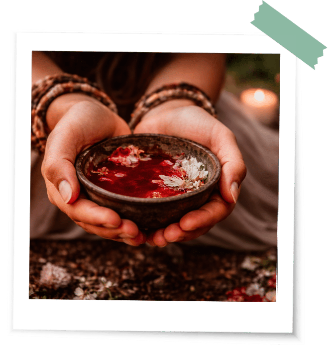 Eine schöne geschmückte Schale mit Blut in Frauenhänden in einem Ritual mit Blüten und Kerzen