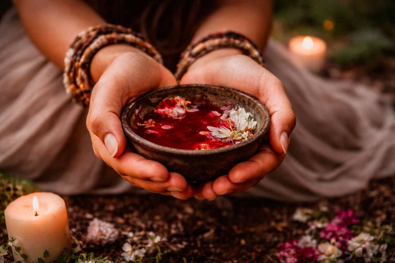 Frauenhände mit einer Schale feiern ein Ritual zu weiblichem Blut mit Blüten und Kerzen
