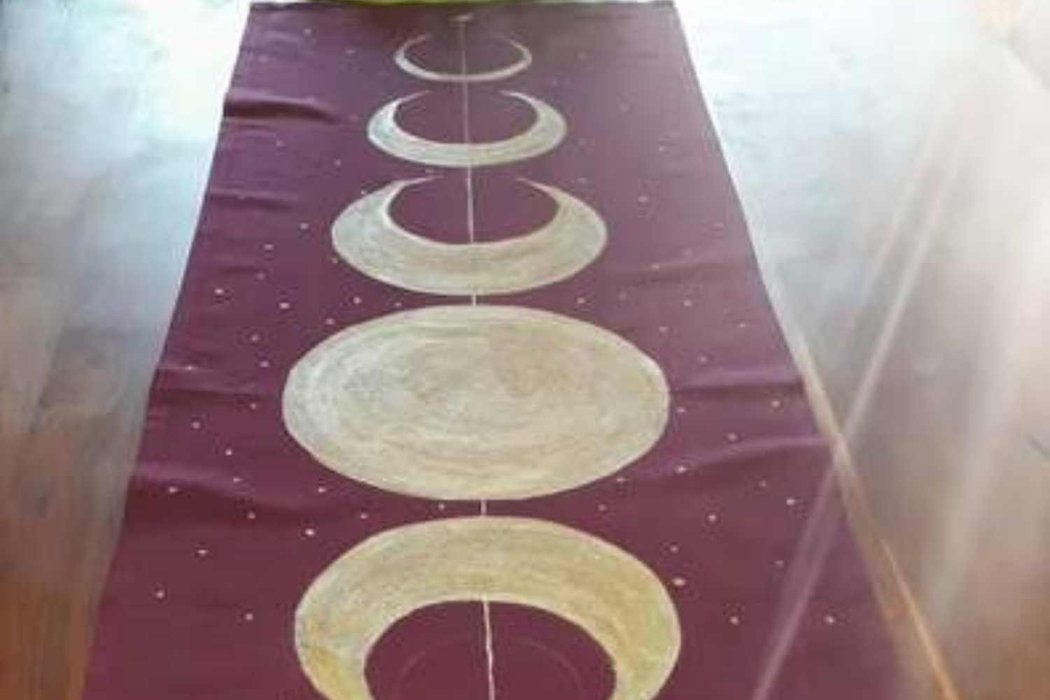 Ein dunkelrotes Tuch mit goldenen Mondphasen bemalt liegt auf einem Holztisch über die Geschichte des ersten LaLuna- Ritualtuchs