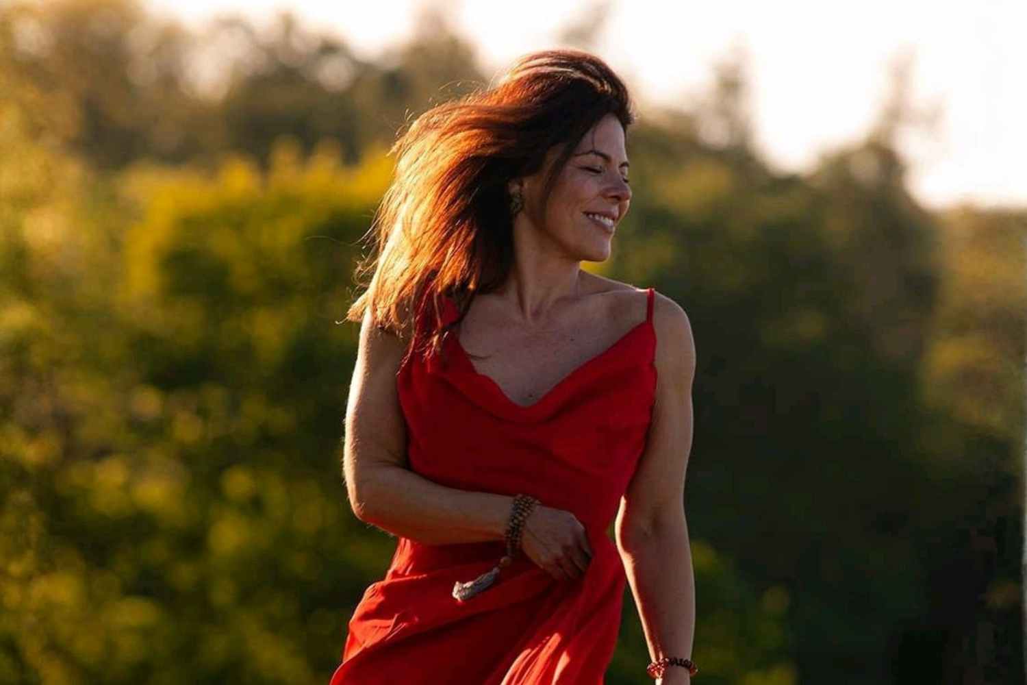 Eine schöne Frau in einem roten Kleib tanzt zu Beltane über eine Wiese in einem lebendigen Ritual