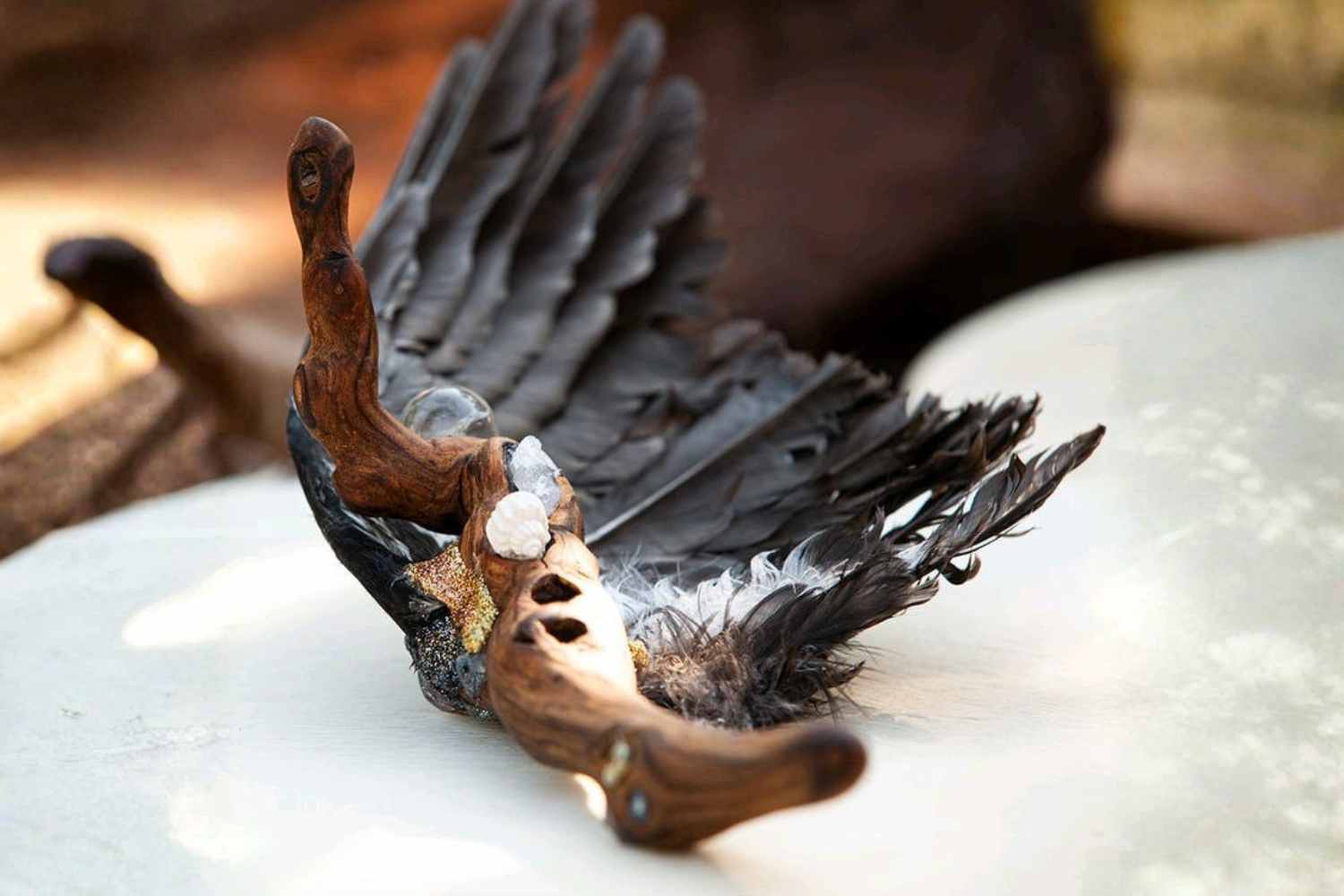 Ein magischer Räucherfächer aus einem Rabenflügel und einer Rebenwurzel liegt auf einem mit Ritualgegenständen geschmückten Tisch