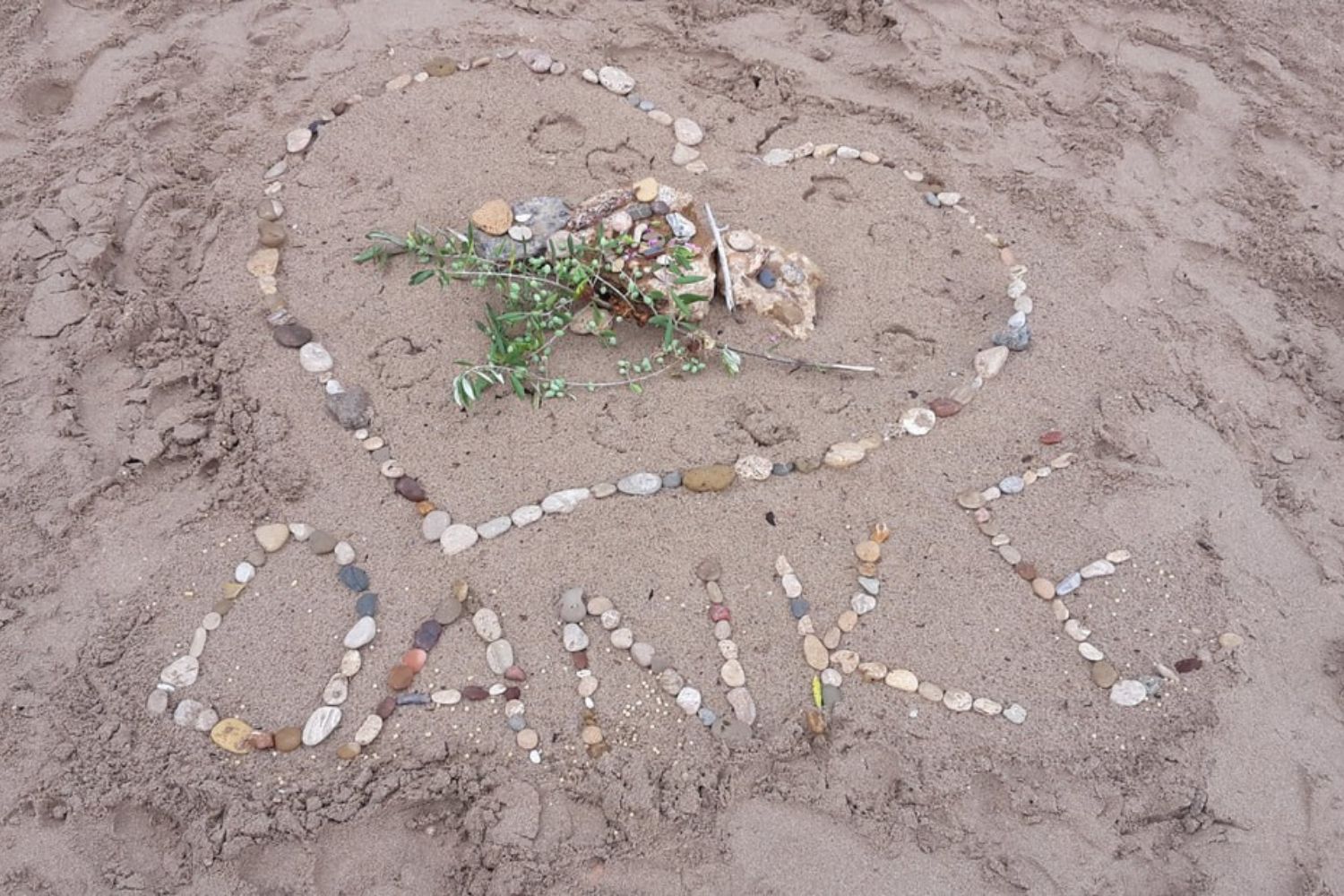 Im Sand gelegtes DANKE aus Steinen als Ausdruck eines persönlichen Dankesrituals am Strand