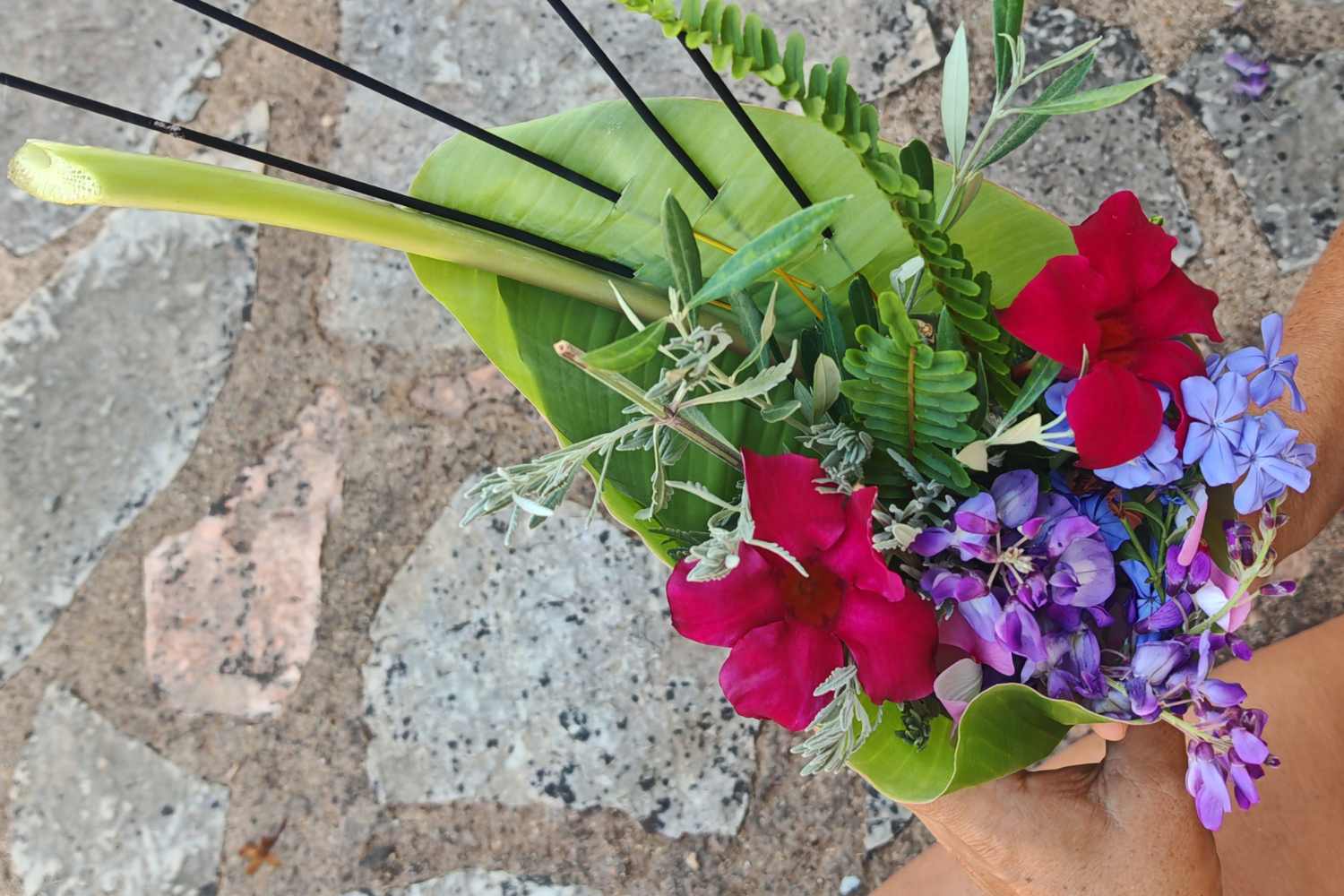 Hand hält selbstgemachte Dankesgabe aus Blättern, Blüten und Räucherwerk als Ritual in der Natur