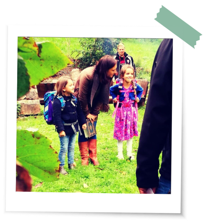 Kinder stehen im Grünen mit Schulranzen bei einem Einschulungsritual