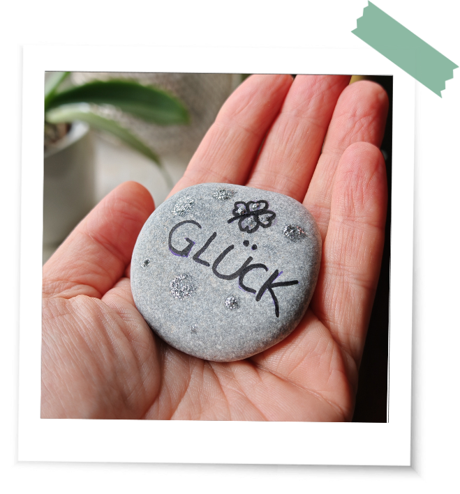 Eine Hand hält einen Stein mit dem Schriftzug "Glück" entstanden in den Rauhnächten