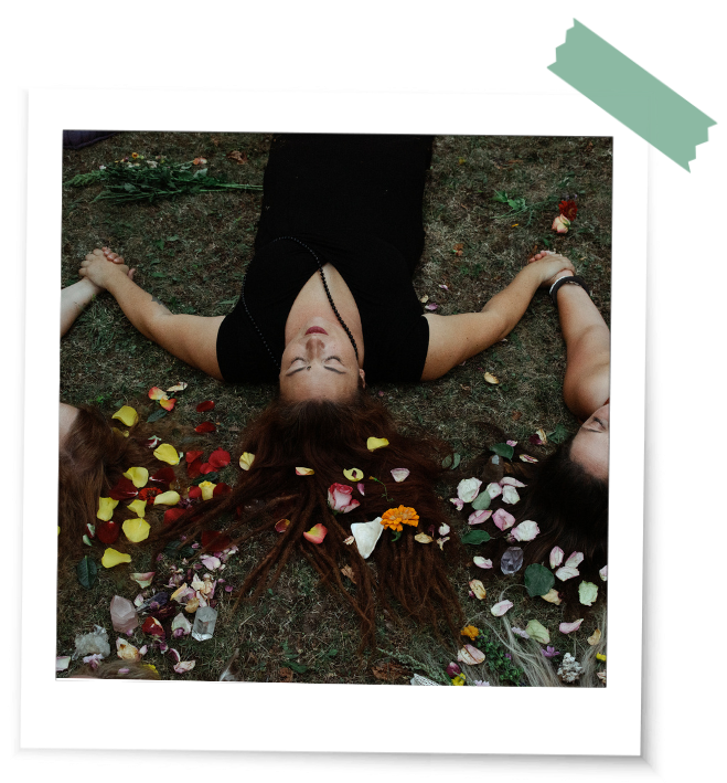 Frauen liegen auf der Erde ihre Haare sind verbunden mit Blüten und rituellen Gegenständen