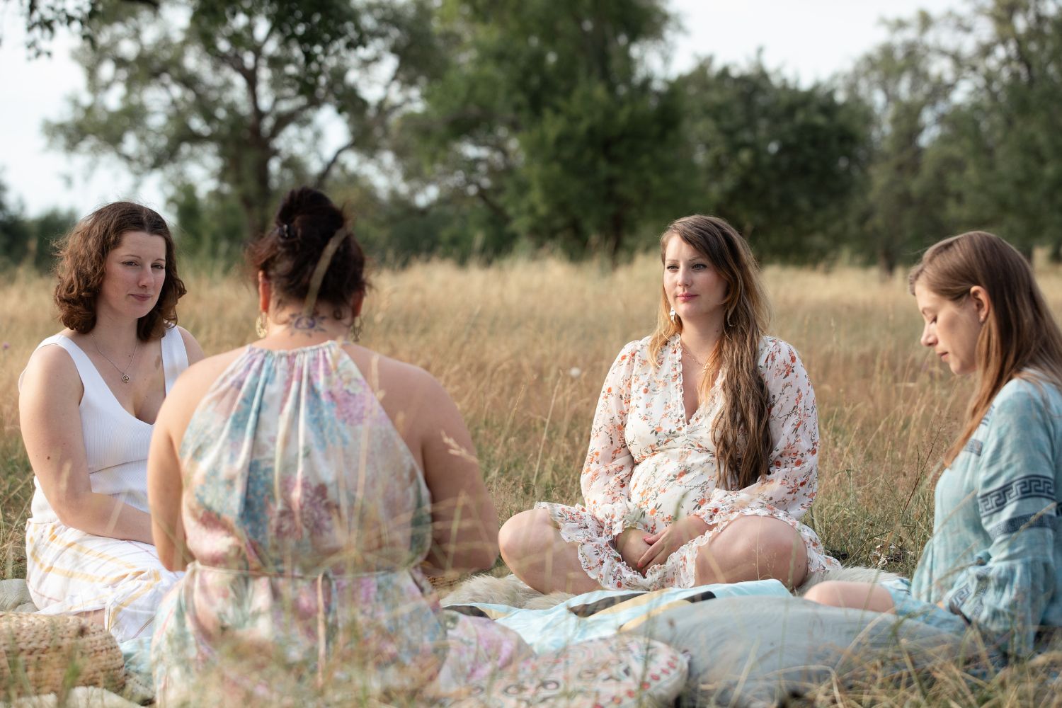Schwangere Frau sitzt im Kreis mit anderen Frauen bei einem Blessingway-Ritual in der Natur
