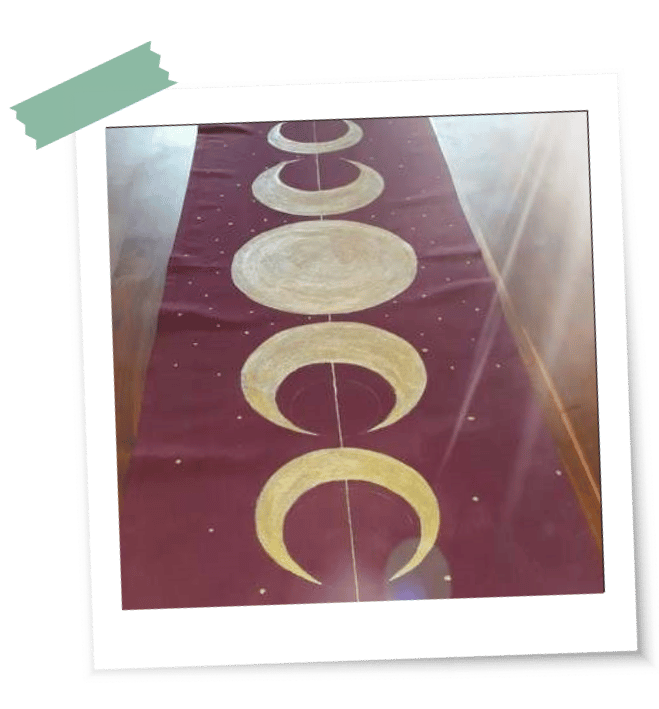 Ein dunkelrotes Tuch mit goldenen Mondphasen liegt auf einem Holztisch als erstes LaLuna-Ritualtuch