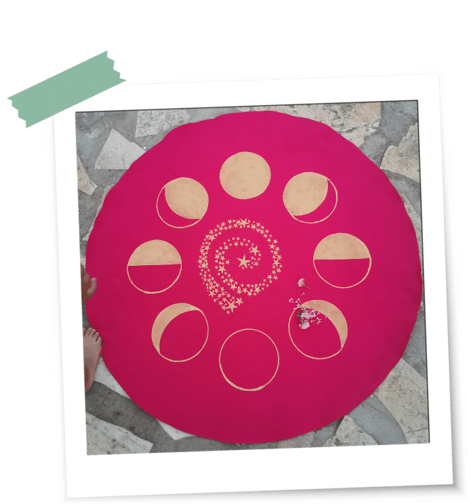 ein pinkfarbenes rundes LaLuna-Ritualtuch liegt auf einem Steinboden mit acht goldenen Mondphasen und einer Sternenspirale in der Mitte