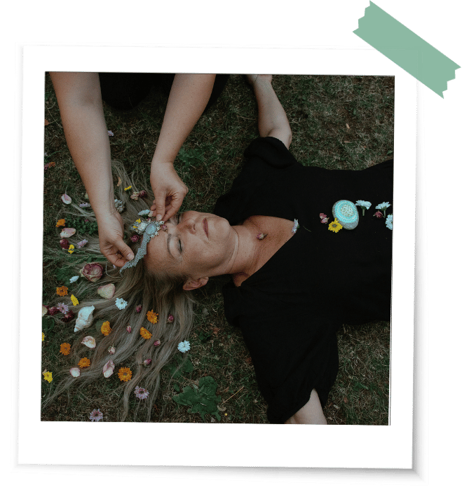 Was ist ein Ritual Haare Frau liegt in einem Ritual am Boden und andere Frauen schmücken ihr Haar mit Muscheln, Edelsteinen und Blumen